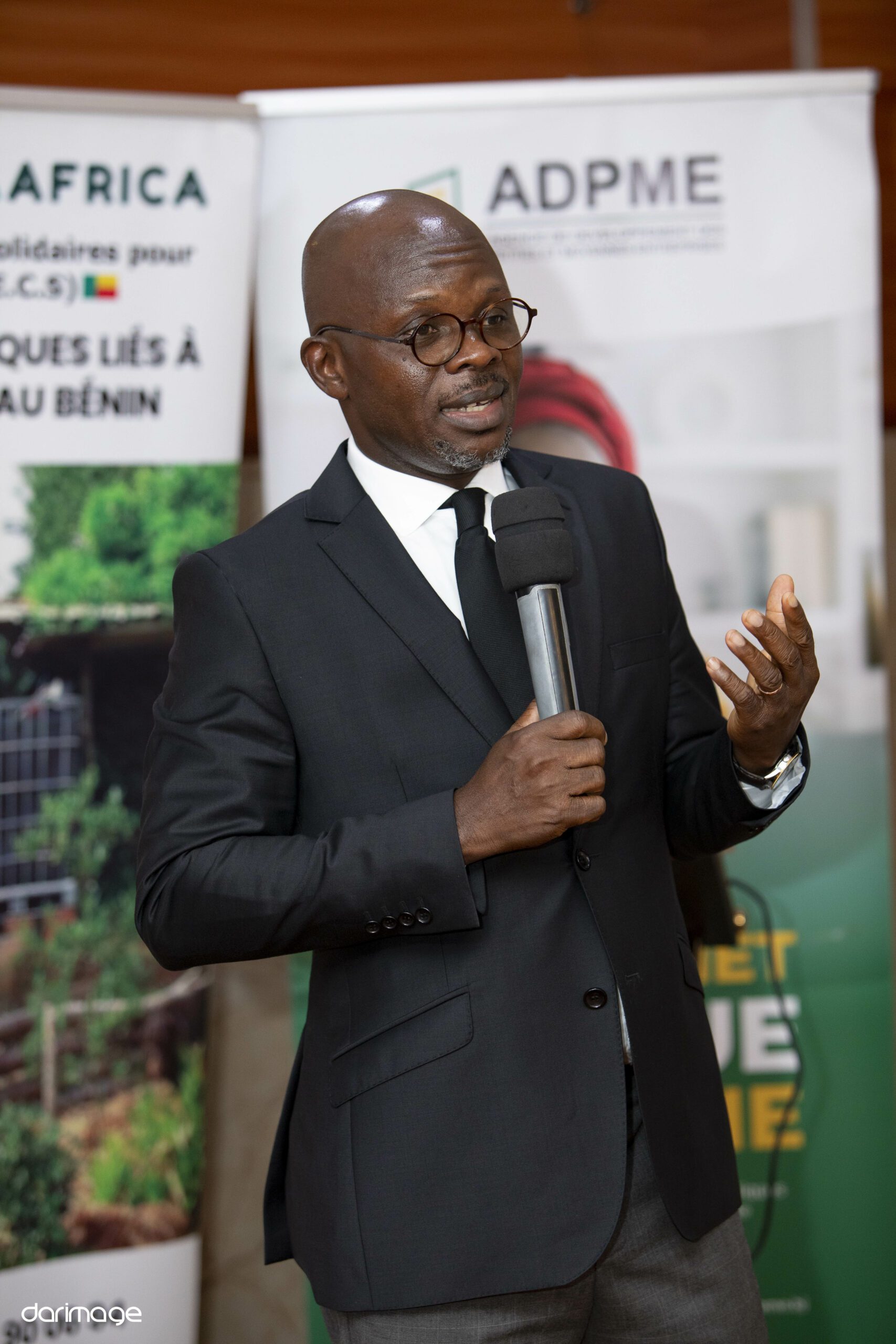 Marcel EFFON, micro en main, s'adresse au public lors du Demo Day national IYBA-SEED, devant les kakémonos de l'ADPME et de TEERRA AFRICA